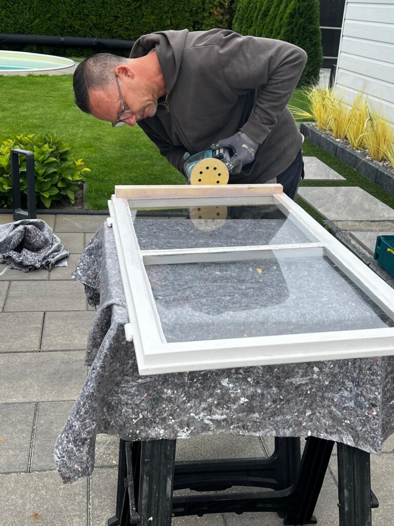 Schleifen der neu eingesetzten Wasserkante an einem Holzfenster während der Reparatur