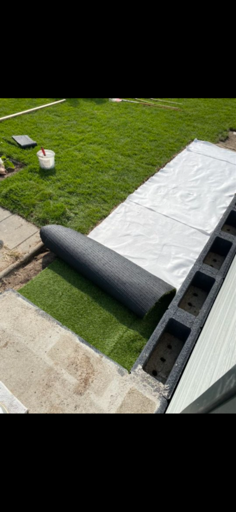 Kunstrasen wird über dem Wurzelschutz entlang des Hauses verlegt